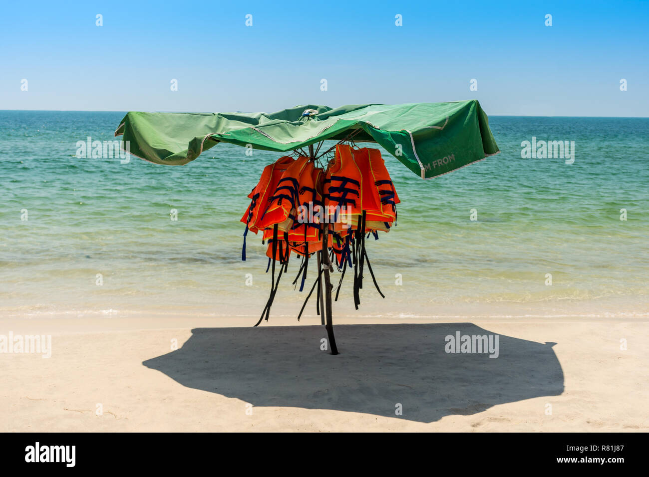 Personal floatation devices shaded from the sun under an umbrella on an empty beach. Stock Photo