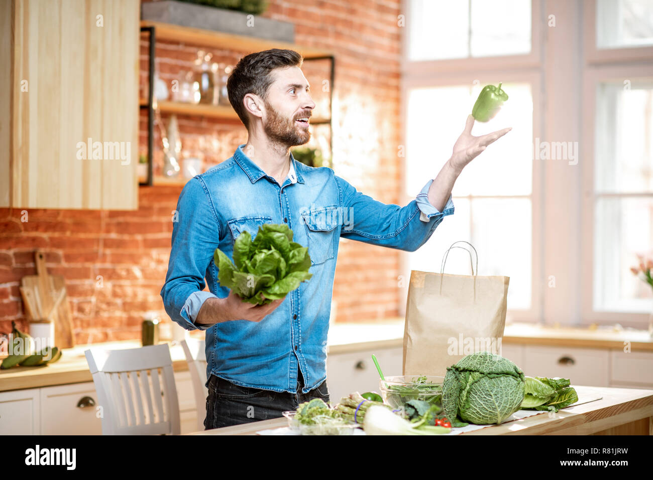 Handsome man throwing up green pepper while cooking vegan meals on the ...