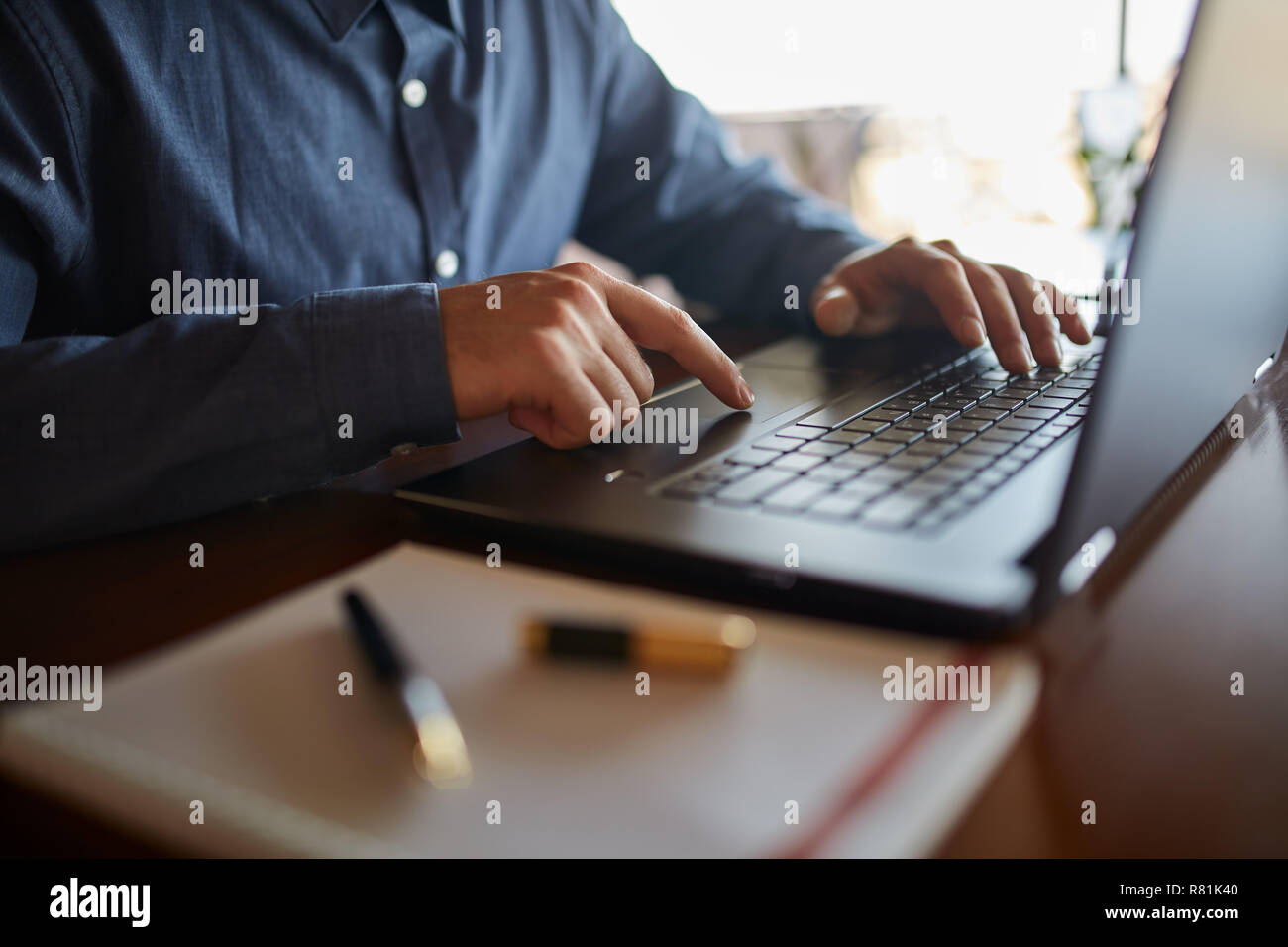 Close-up photo of caucasian male hands typing on laptop keyboard and using  touchpad. Notebook and pen on foreground of workspace. Business man working  on computer. Isolated no face view Stock Photo -