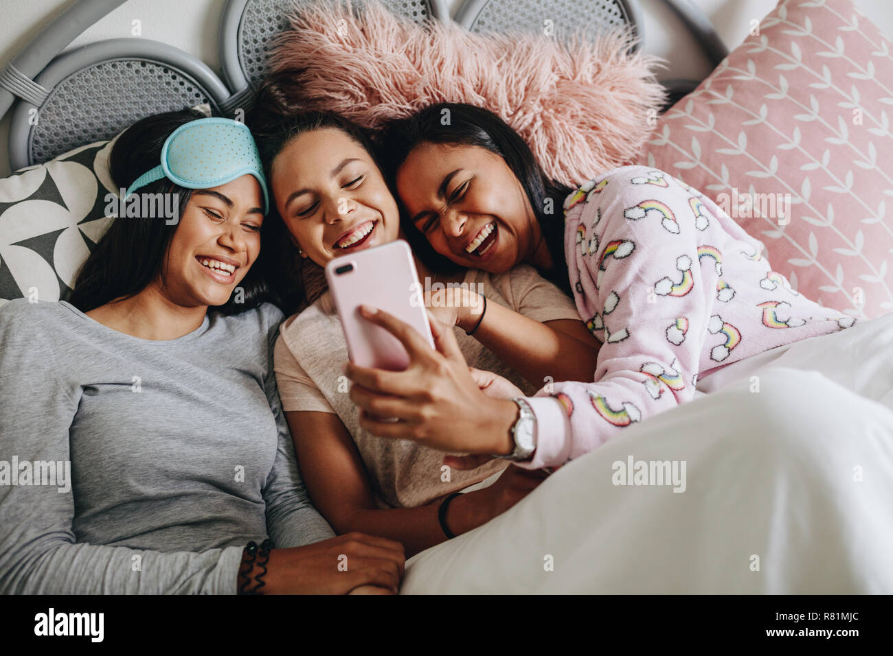 Three young girls watching a movie on mobile phone lying on bed during a  sleepover. Girl friends lying on bed laughing while looking at a mobile  phone Stock Photo - Alamy