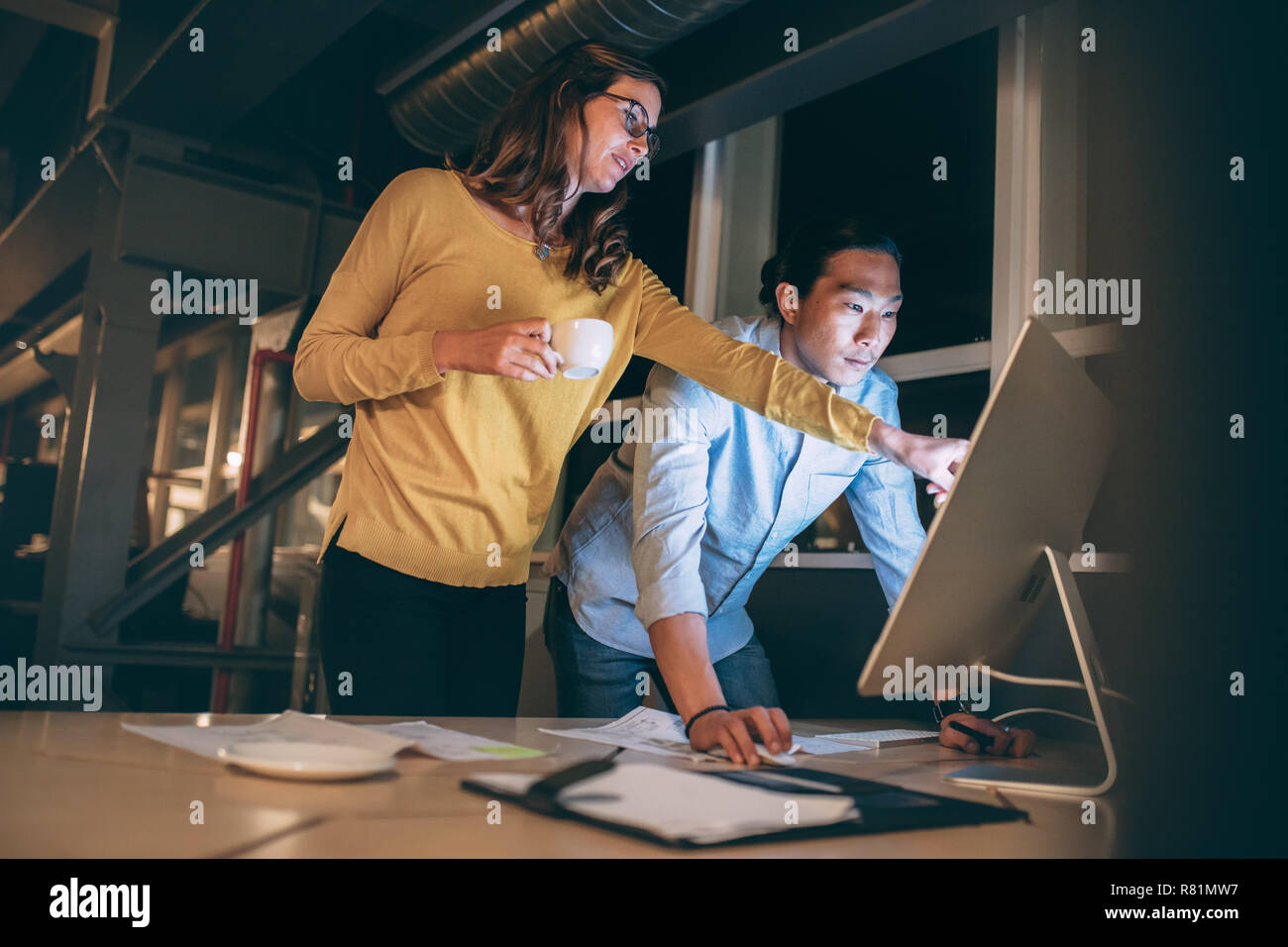 business colleagues discussing business work late in office. Woman entrepreneur pointing at the computer screen explaining to her business partner. Stock Photo