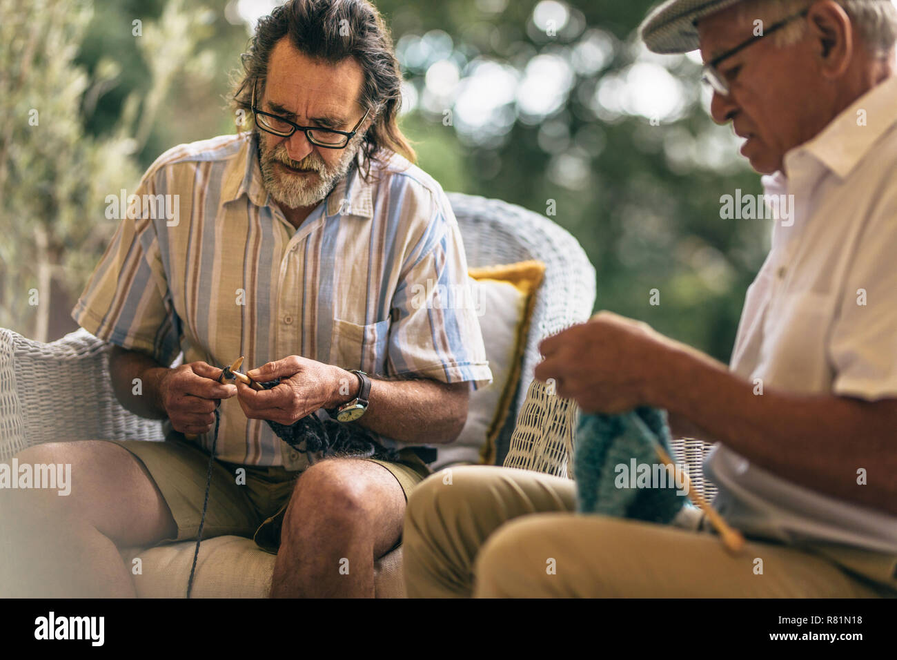 Two elderly men learning knitting at old age. Retired male friends doing knitting to pastime at home. Stock Photo