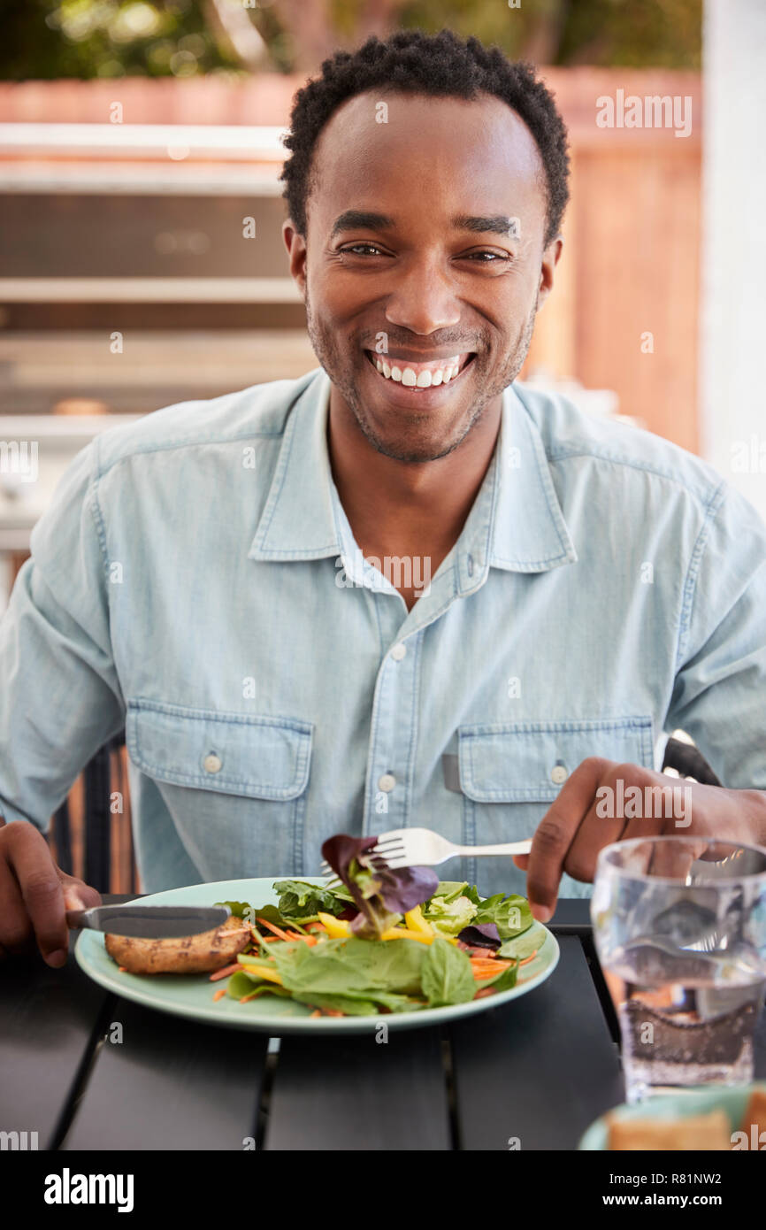 Young black man eating lunch at a table outside, vertical Stock Photo