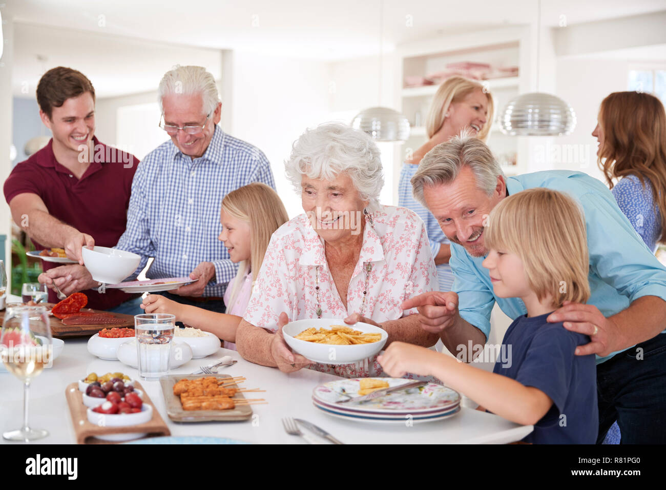 Multi-Generation Family And Friends Eating Food In Kitchen At Celebration Party Stock Photo