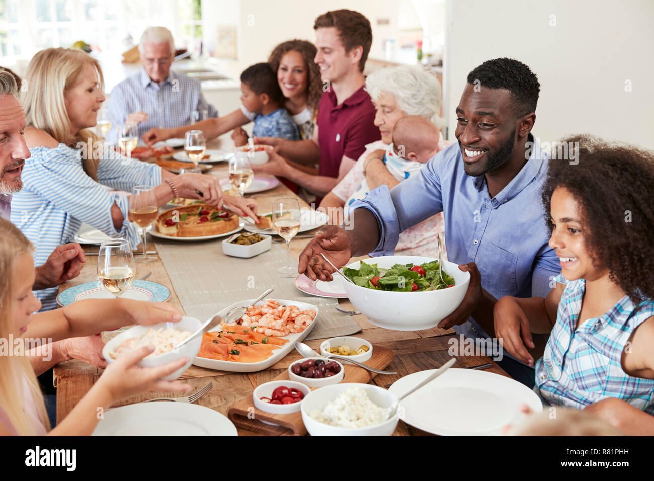 Group Of Multi-Generation Family And Friends Sitting Around Table And Enjoying Meal Stock Photo