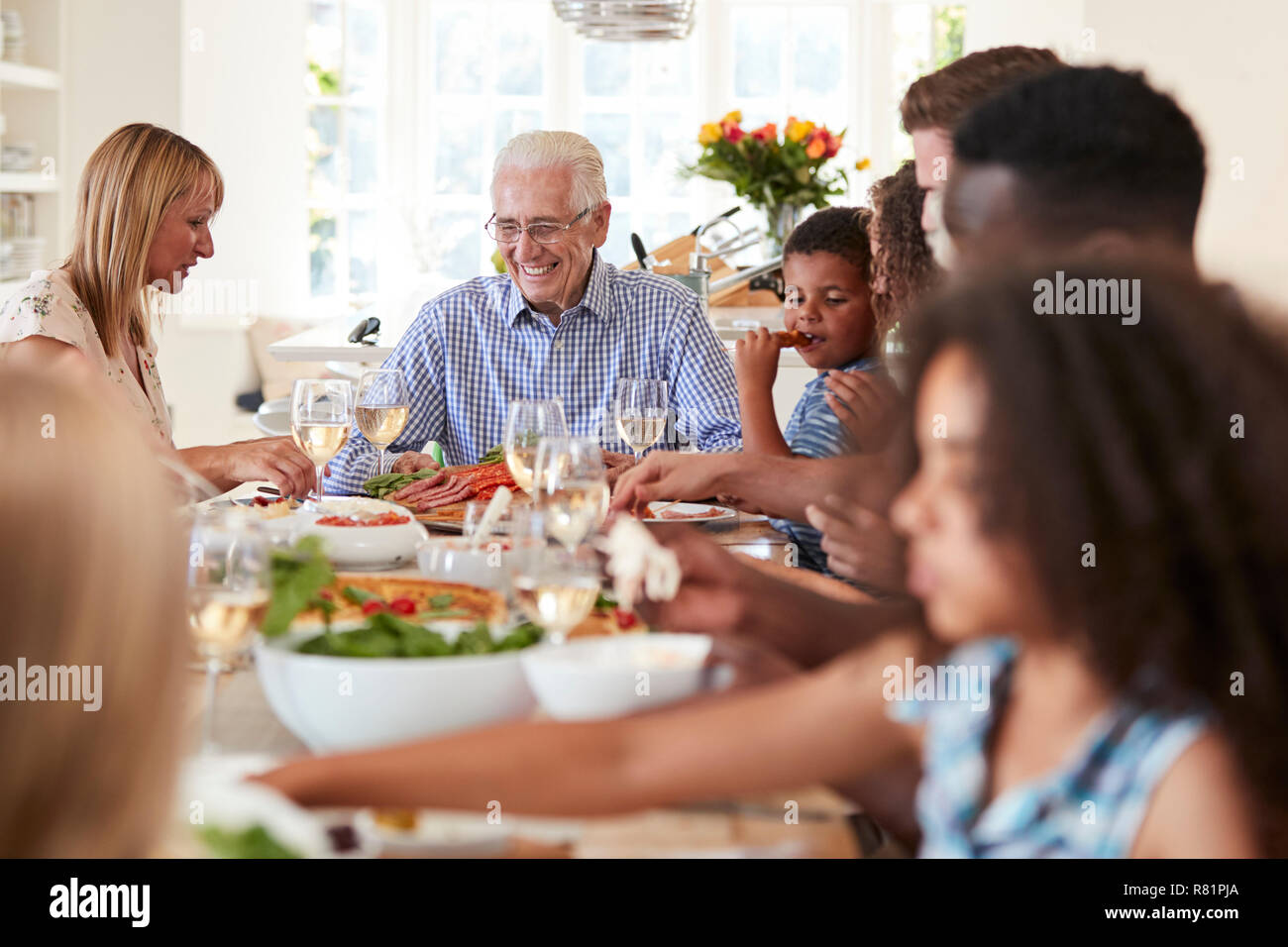 Group Of Multi-Generation Family And Friends Sitting Around Table And Enjoying Meal Stock Photo