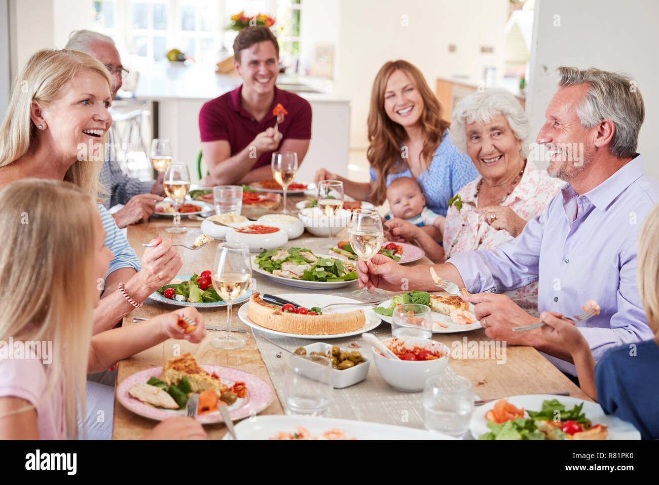 Group Of Multi-Generation Family And Friends Sitting Around Table And Making A Toast Stock Photo