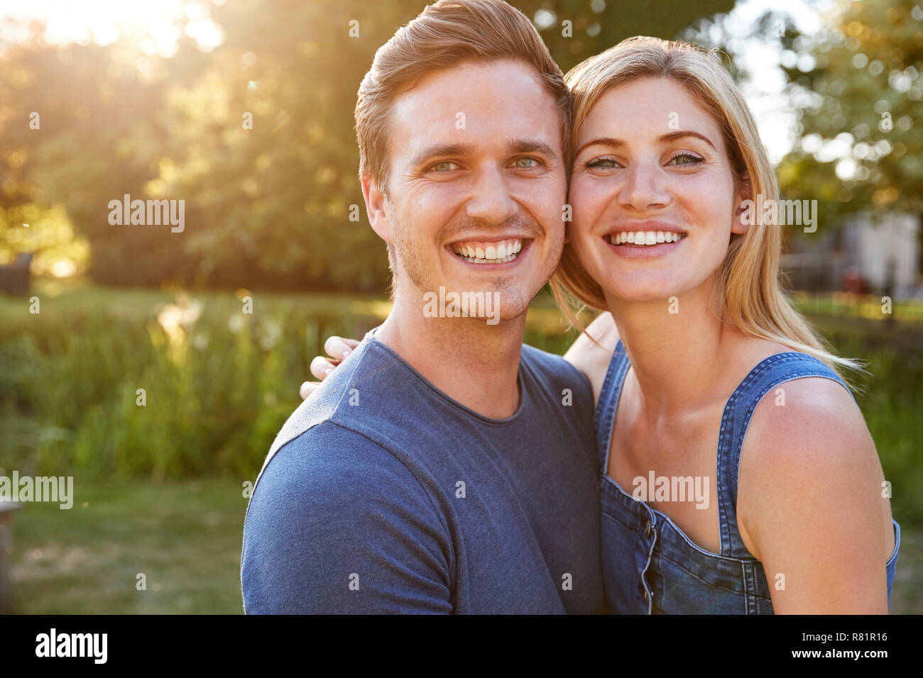 Portrait Of Smiling Couple Outdoors In Summer Park Against Flaring Sun Stock Photo