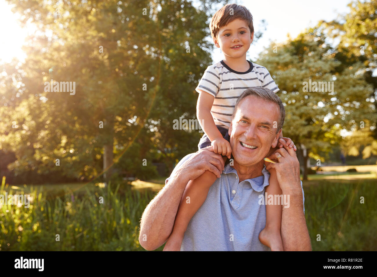Portrait Of Grandfather Giving Grandson Ride On Shoulders In Summer Park Stock Photo