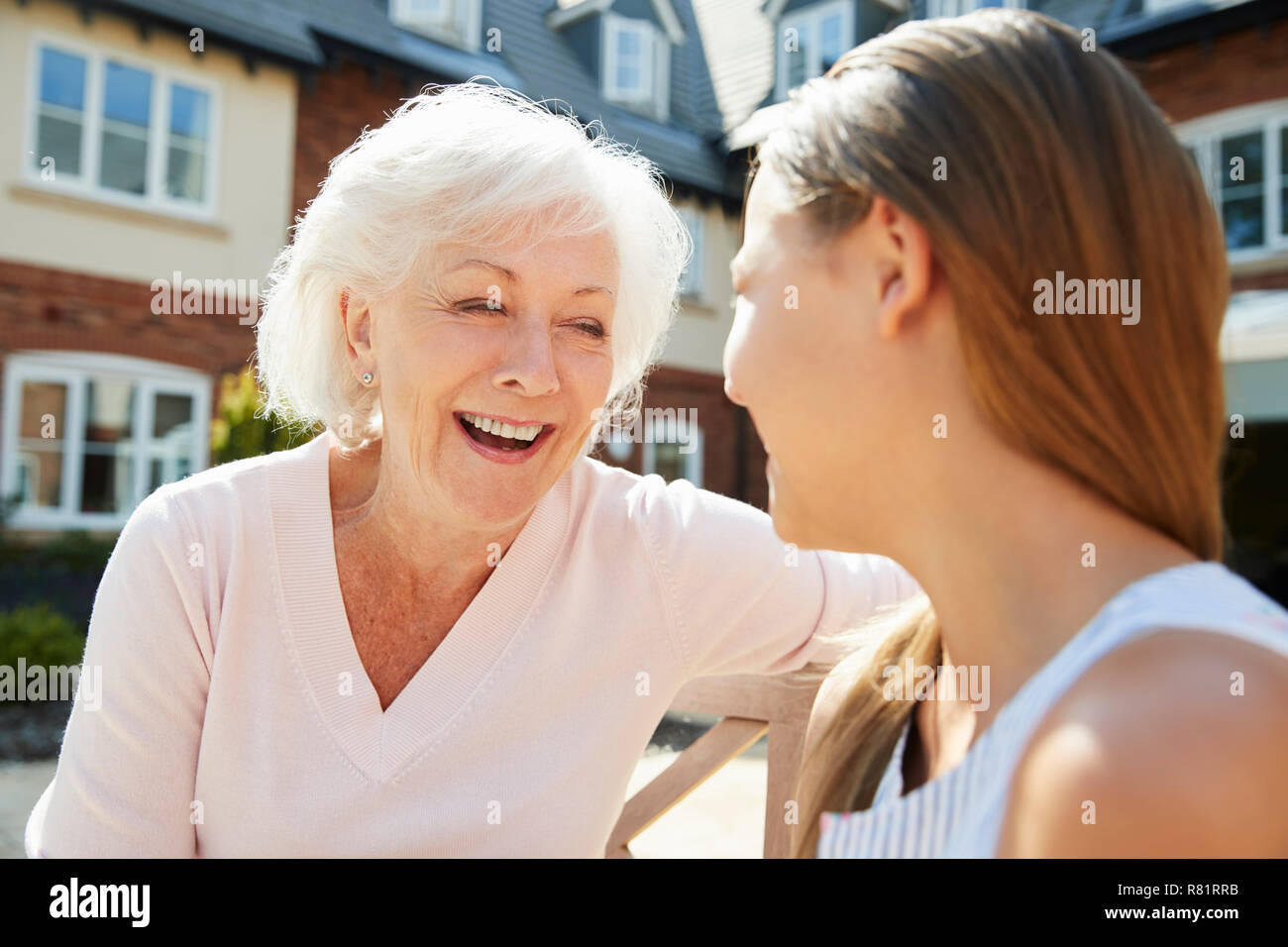 Granddaughter Sitting On Bench With Grandmother During Visit To Retirement Home Stock Photo