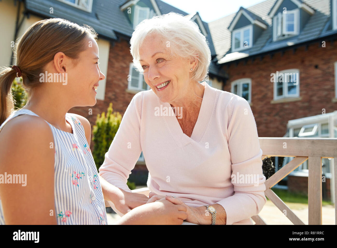 Granddaughter Sitting On Bench With Grandmother During Visit To Retirement Home Stock Photo