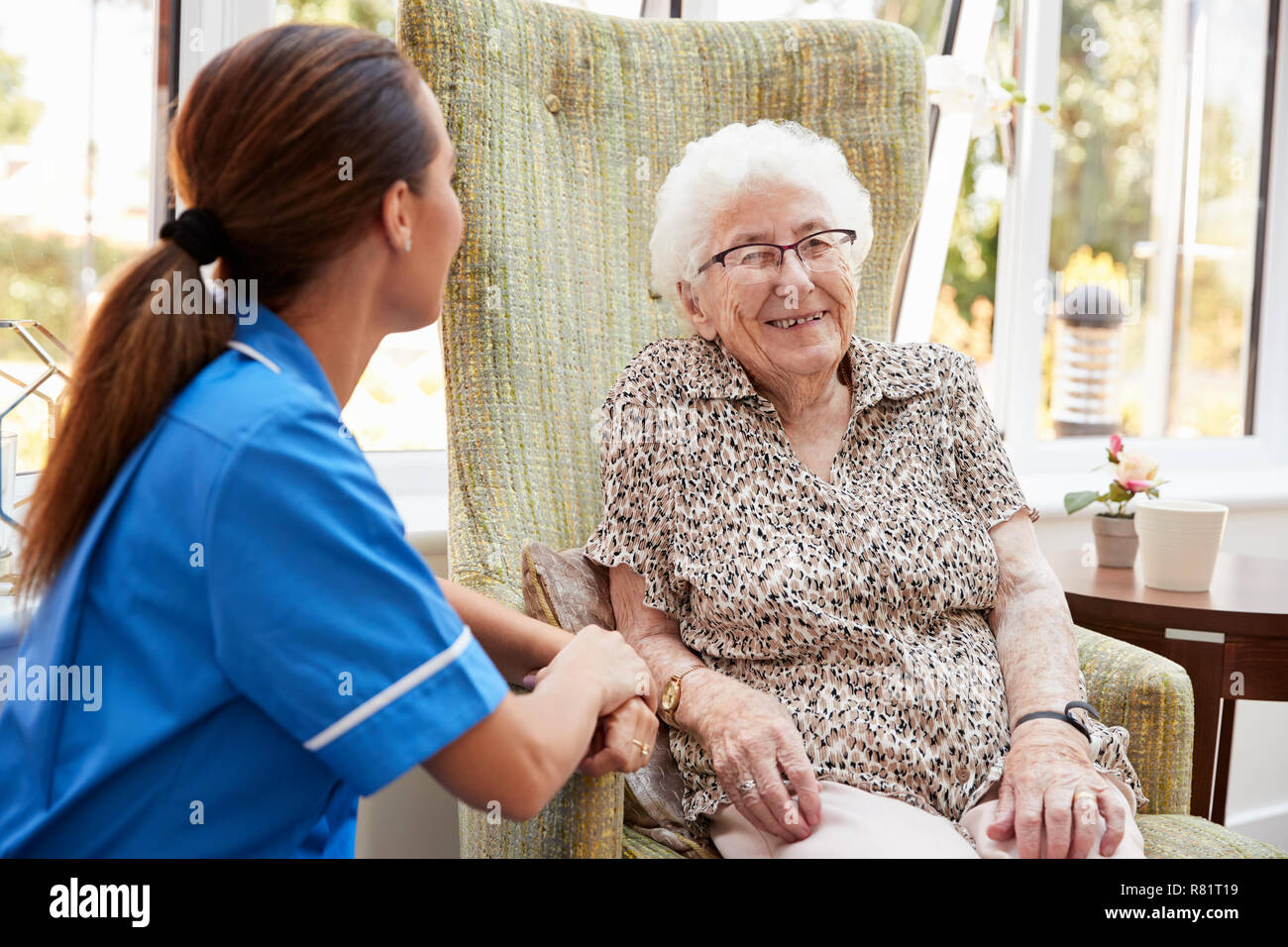 Senior Woman Sitting In Chair And Talking With Nurse In Retirement Home Stock Photo