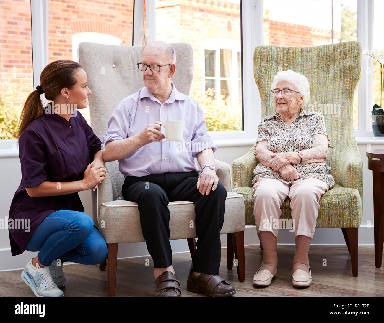 Male And Female Residents Sitting In Chair And Talking With Carer In Retirement Home Stock Photo
