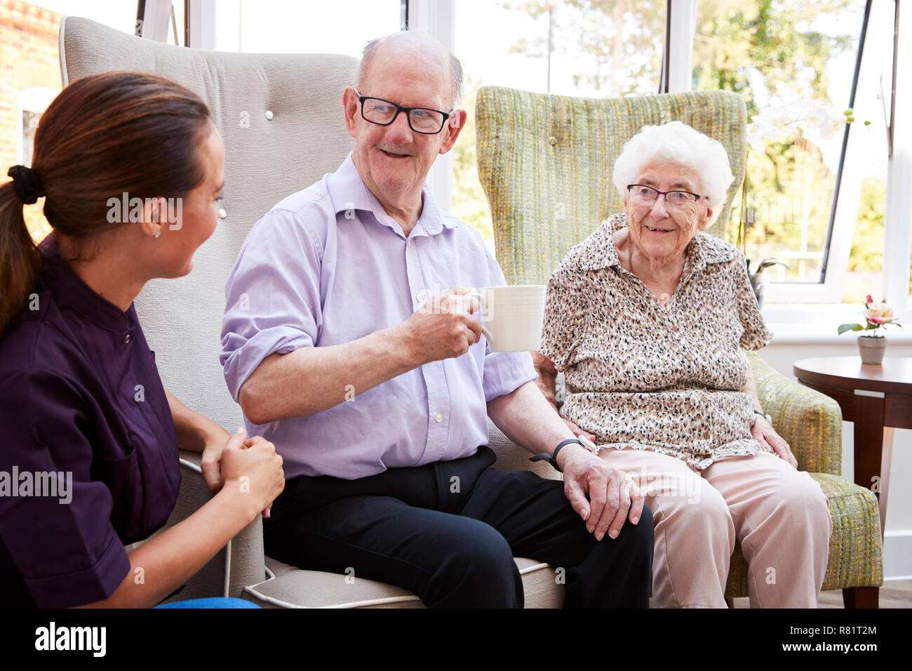 Male And Female Residents Sitting In Chair And Talking With Carer In Retirement Home Stock Photo