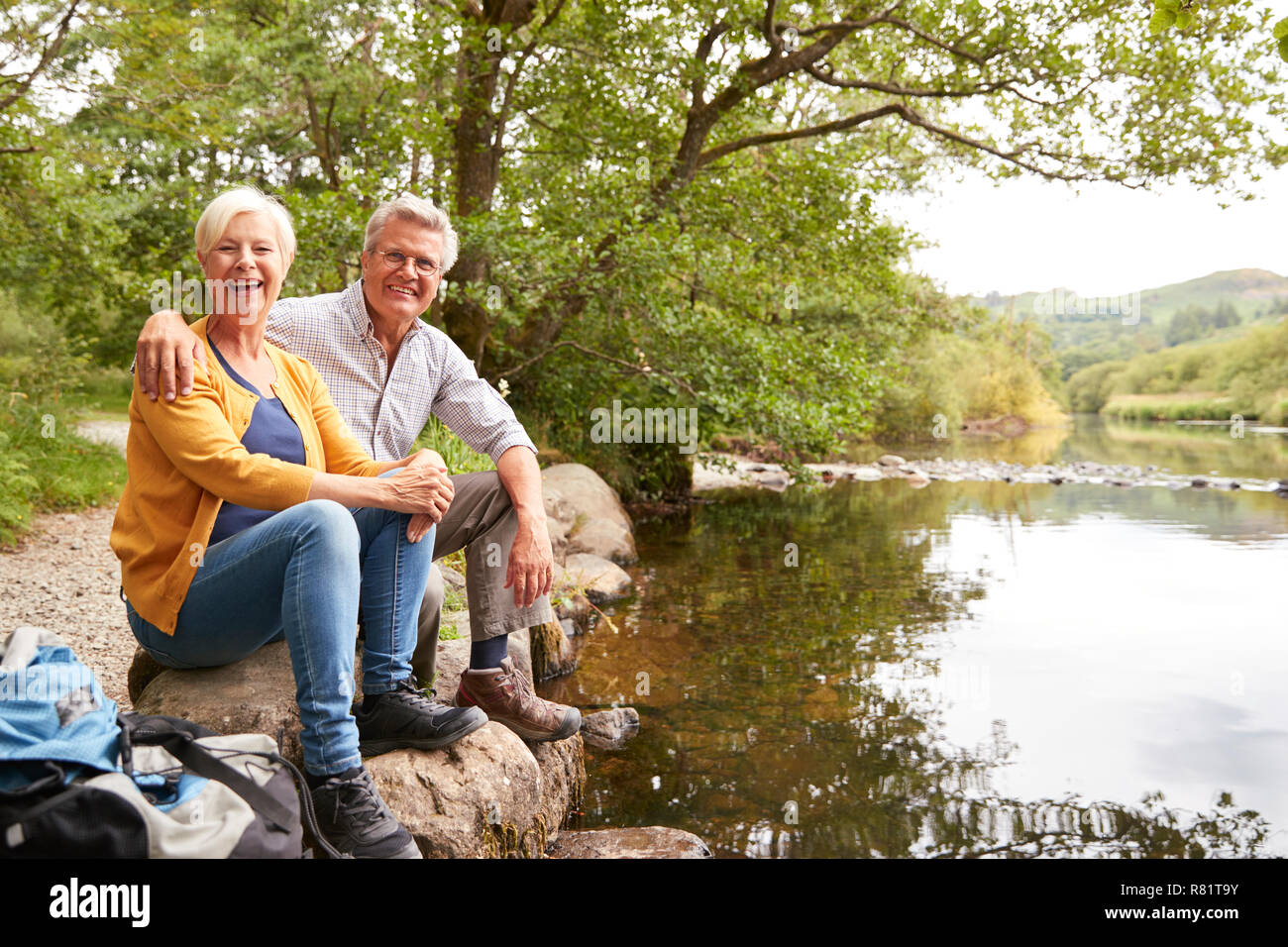 Portrait Of Senior Couple On Hike Sitting By River In UK Lake District Stock Photo