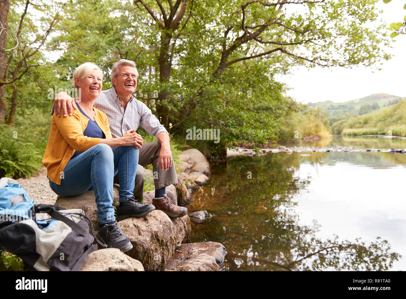 Senior Couple On Hike Sitting By River In UK Lake District Stock Photo