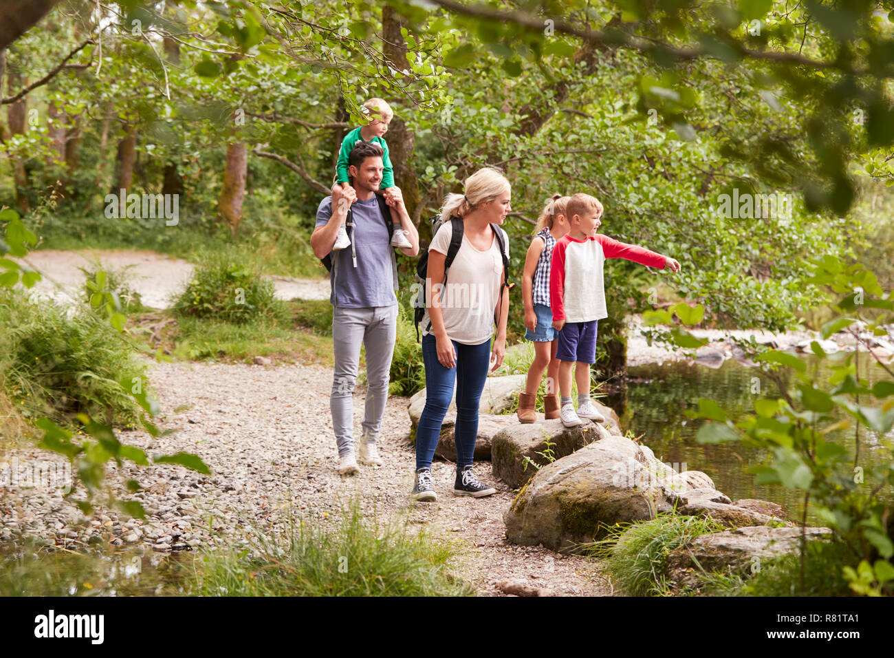 Family Hiking Along Path By River In UK Lake District Stock Photo