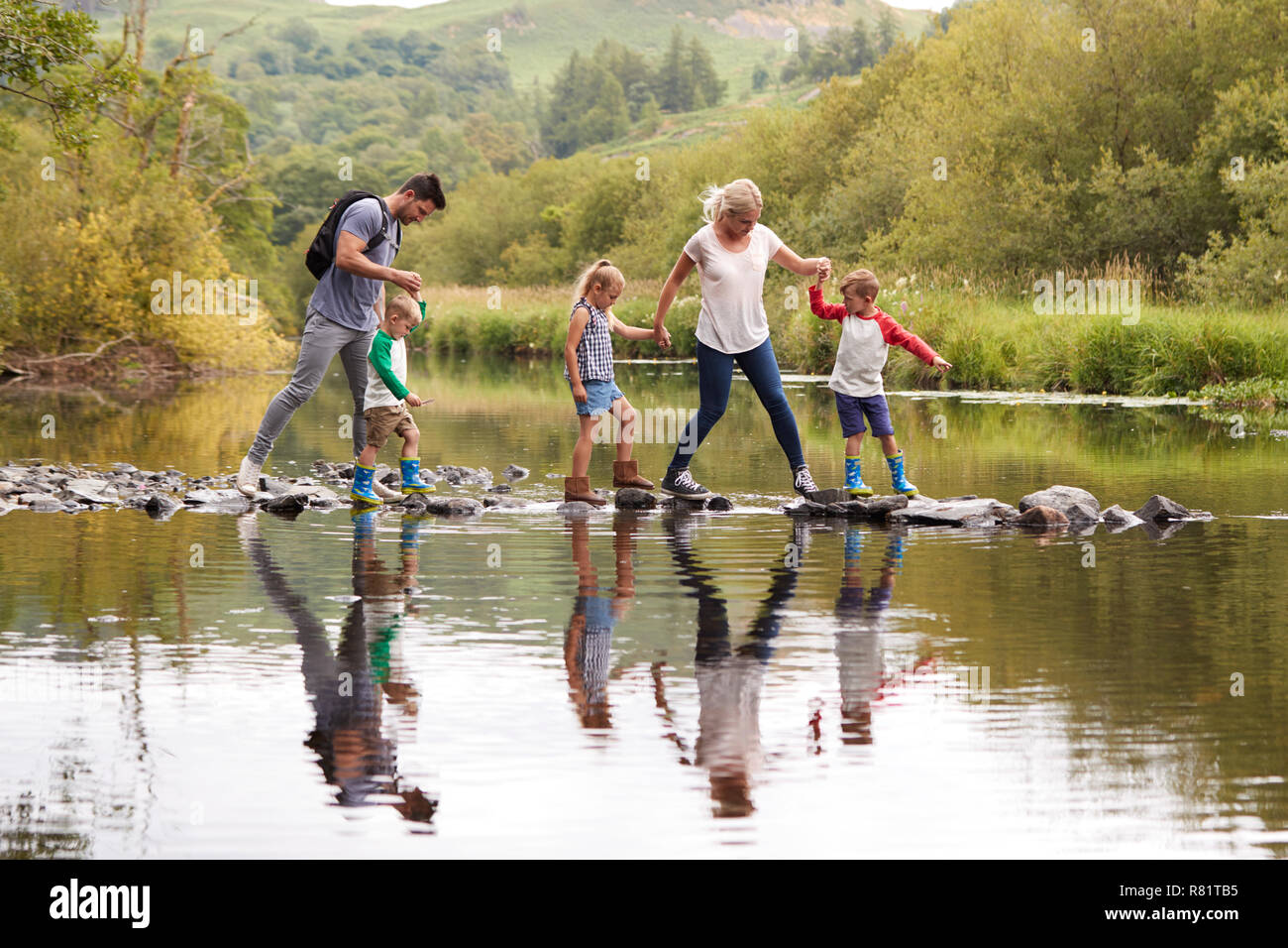 Family Crossing River Whilst Hiking In UK Lake District Stock Photo