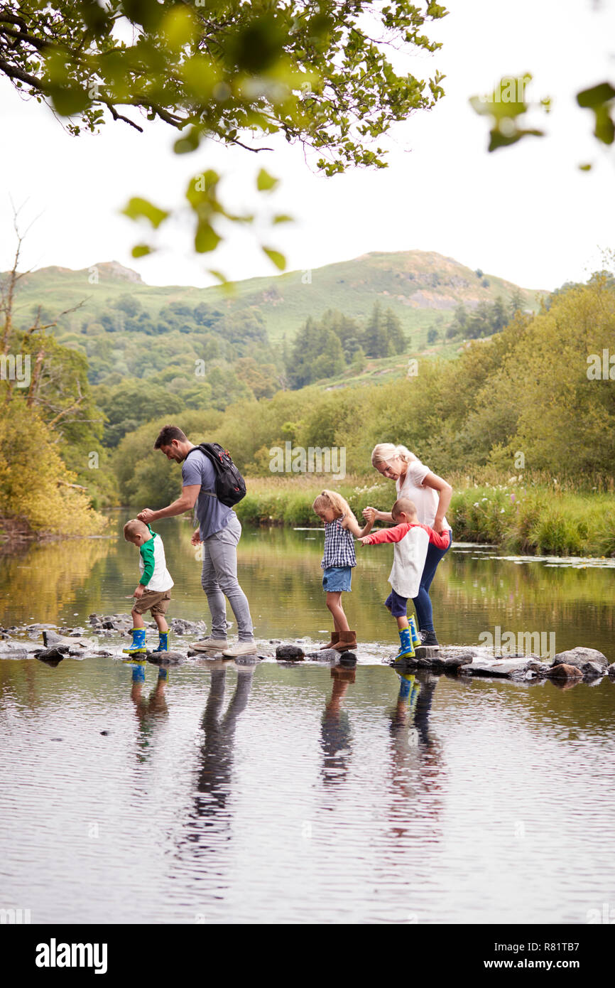 Family Crossing River Whilst Hiking In UK Lake District Stock Photo