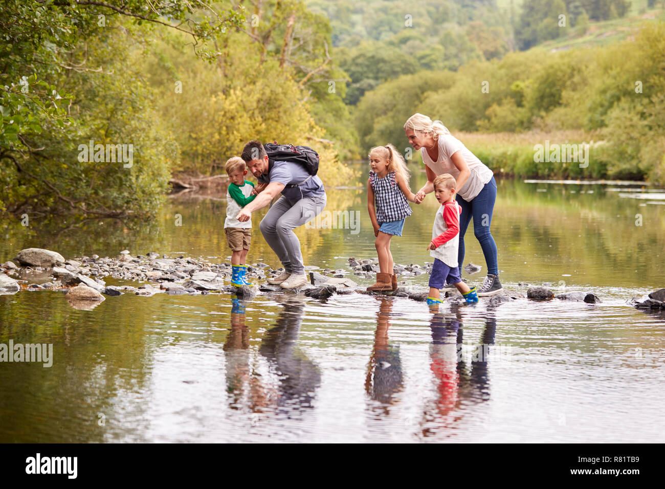 Family Crossing River Whilst Hiking In UK Lake District Stock Photo