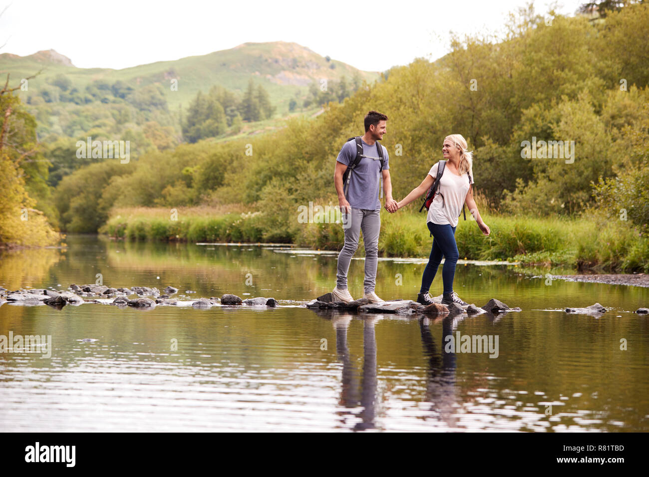 Couple Crossing River Whilst Hiking In UK Lake District Stock Photo