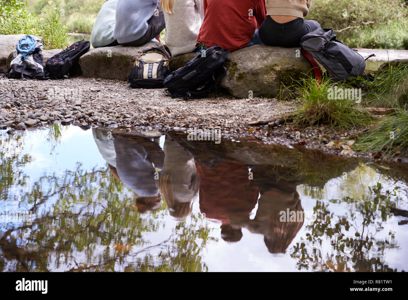 Reflection in stream of five young adult friends taking a break sitting ...