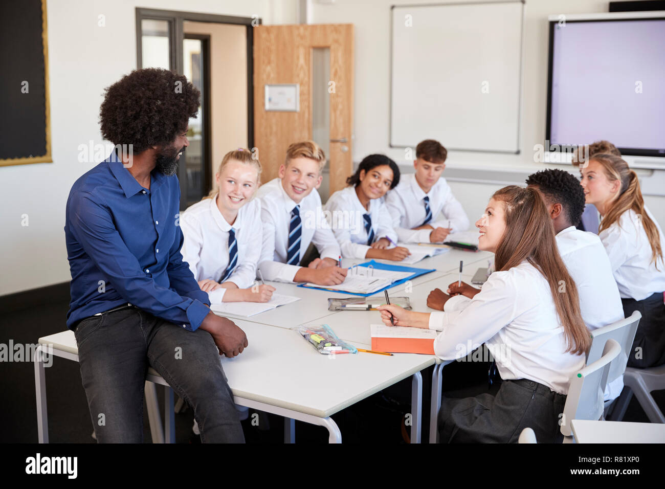 Male High School Teacher Sitting At Table With Teenage Pupils Wearing Uniform Teaching Lesson Stock Photo