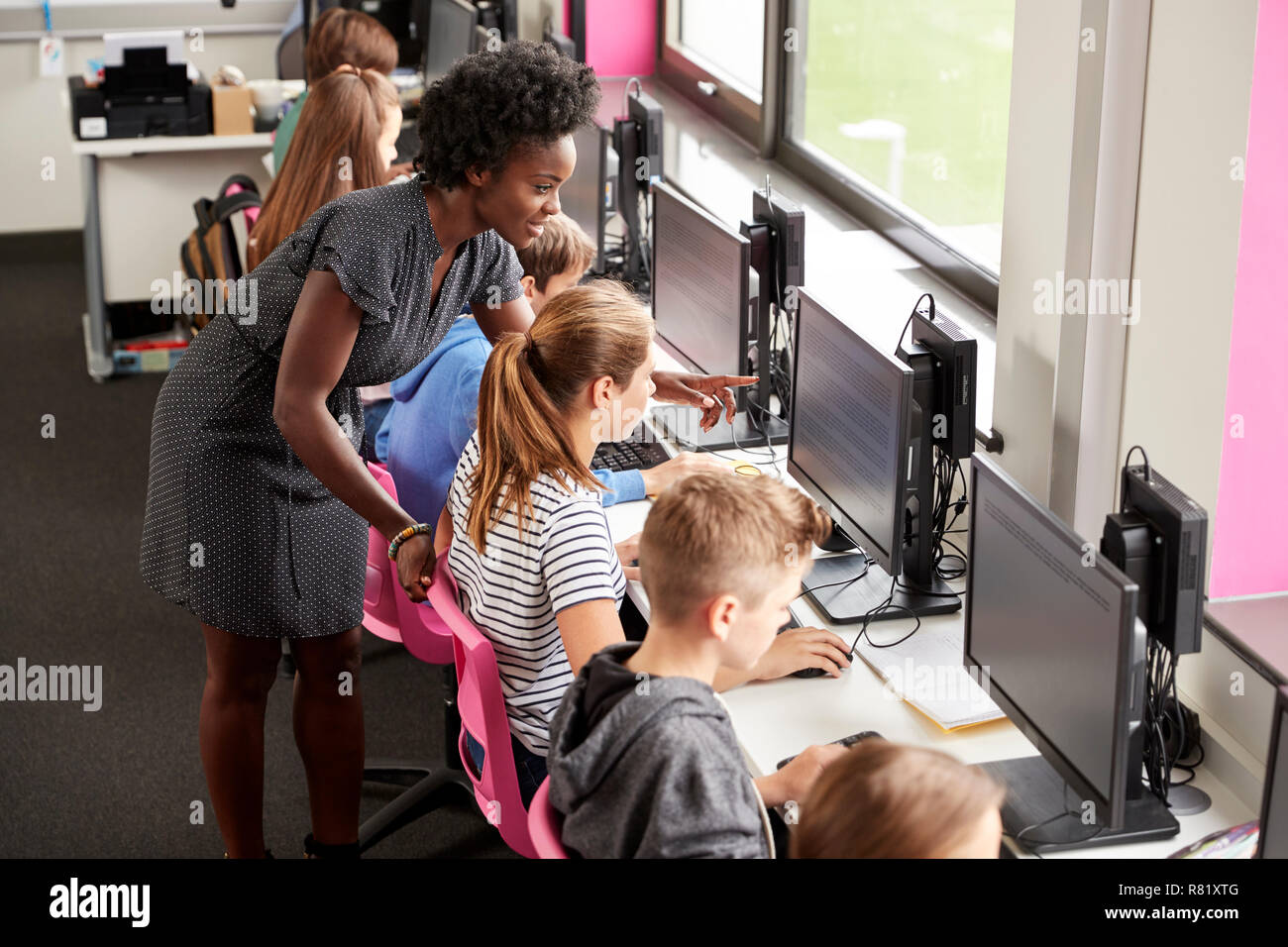 Teacher Helping Female Pupil Line Of High School Students Working at Screens In Computer Class Stock Photo
