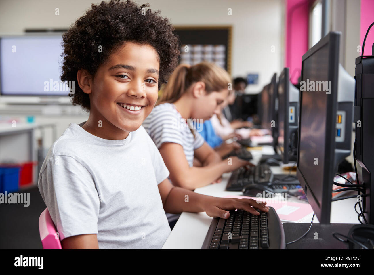 Portrait Of Smiling Male Pupil Sitting In Line Of High School Students Working at Screens In Computer Class Stock Photo