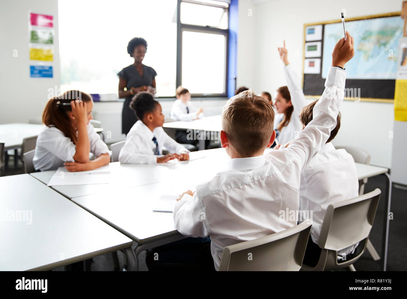 High School Students Wearing Uniform Raising Hands To Answer Question Set By Teacher In Classroom Stock Photo