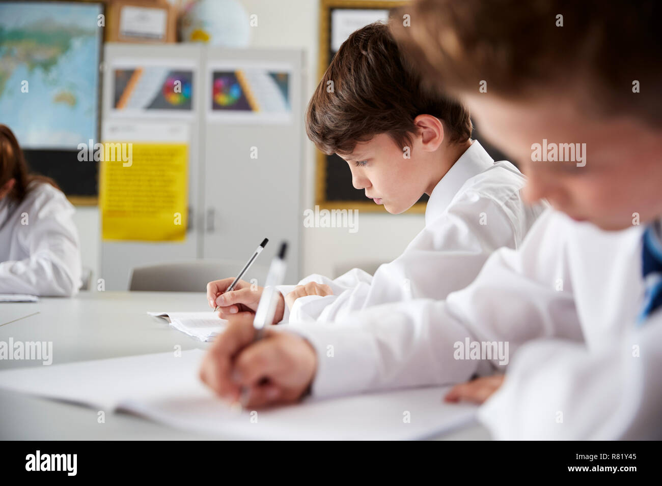 High School Students Wearing Uniform Sitting And Working Around Table In Lesson Stock Photo