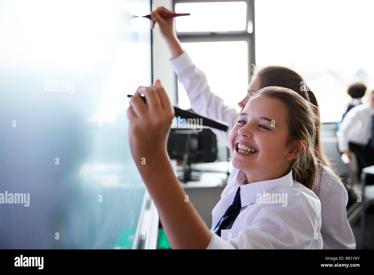 Female High School Students Wearing Uniform Using Interactive Whiteboard During Lesson Stock Photo