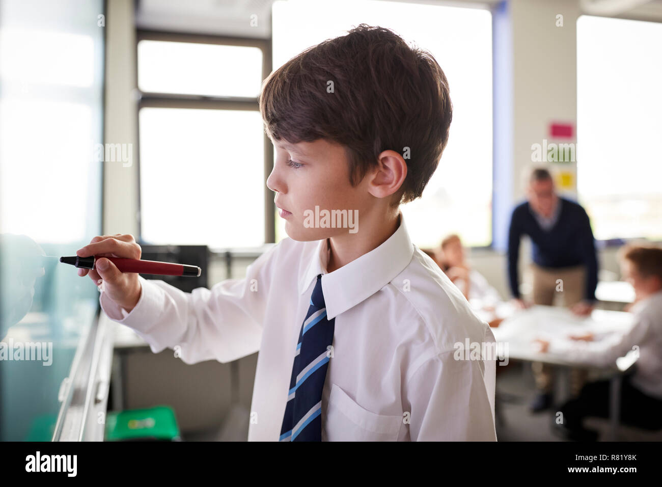 Male High School Student Wearing Uniform Using Interactive Whiteboard During Lesson Stock Photo