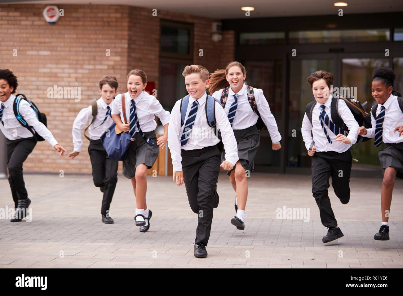 Group Of High School Students Wearing Uniform Running Out Of School Buildings Towards Camera At The End Of Class Stock Photo