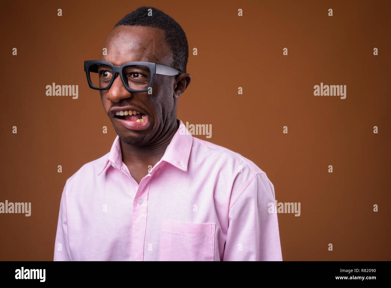 Portrait of young African businessman making faces against brown background Stock Photo