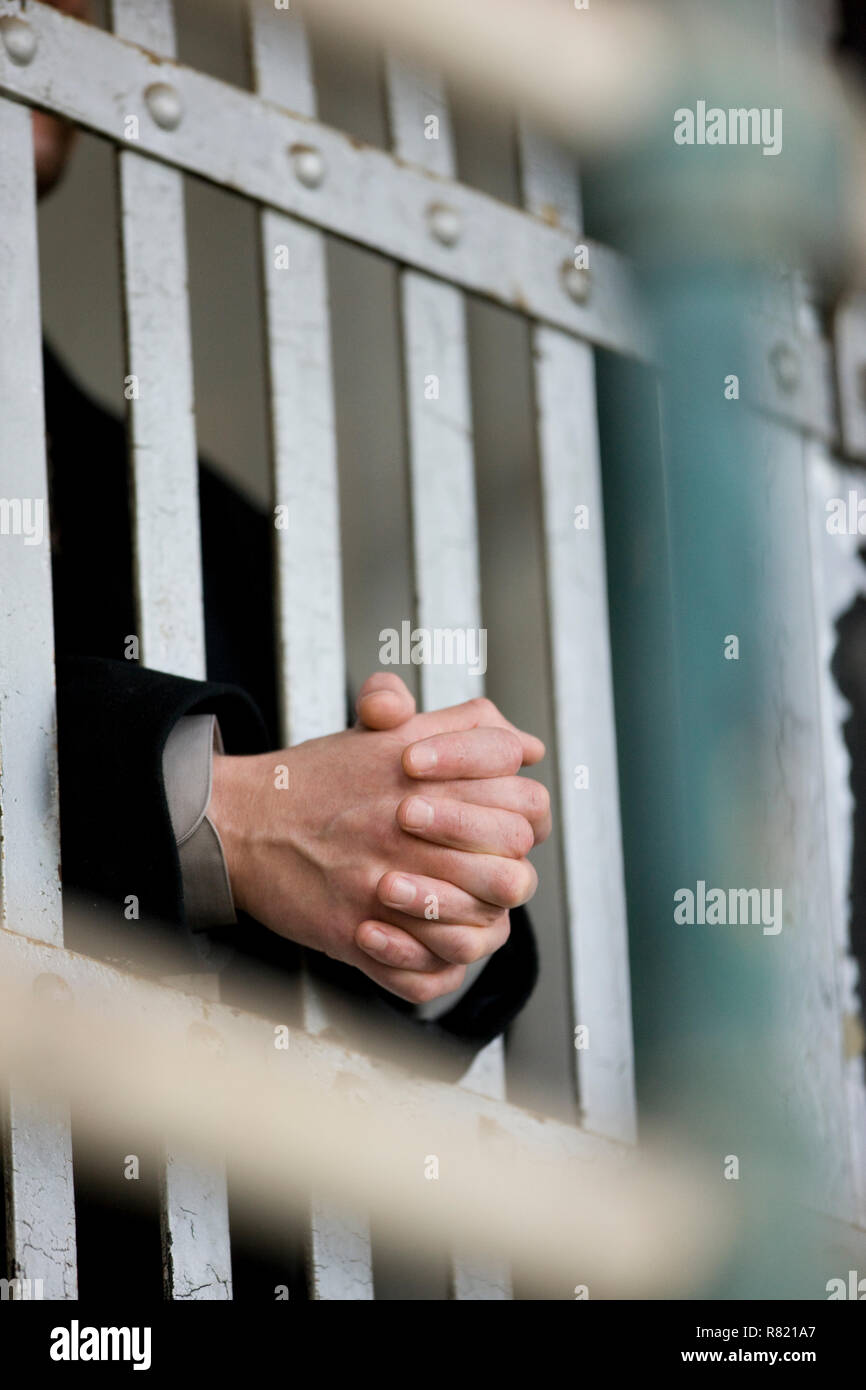 Hands of a young adult businessman through bars of a prison cell in a derelict building. Stock Photo