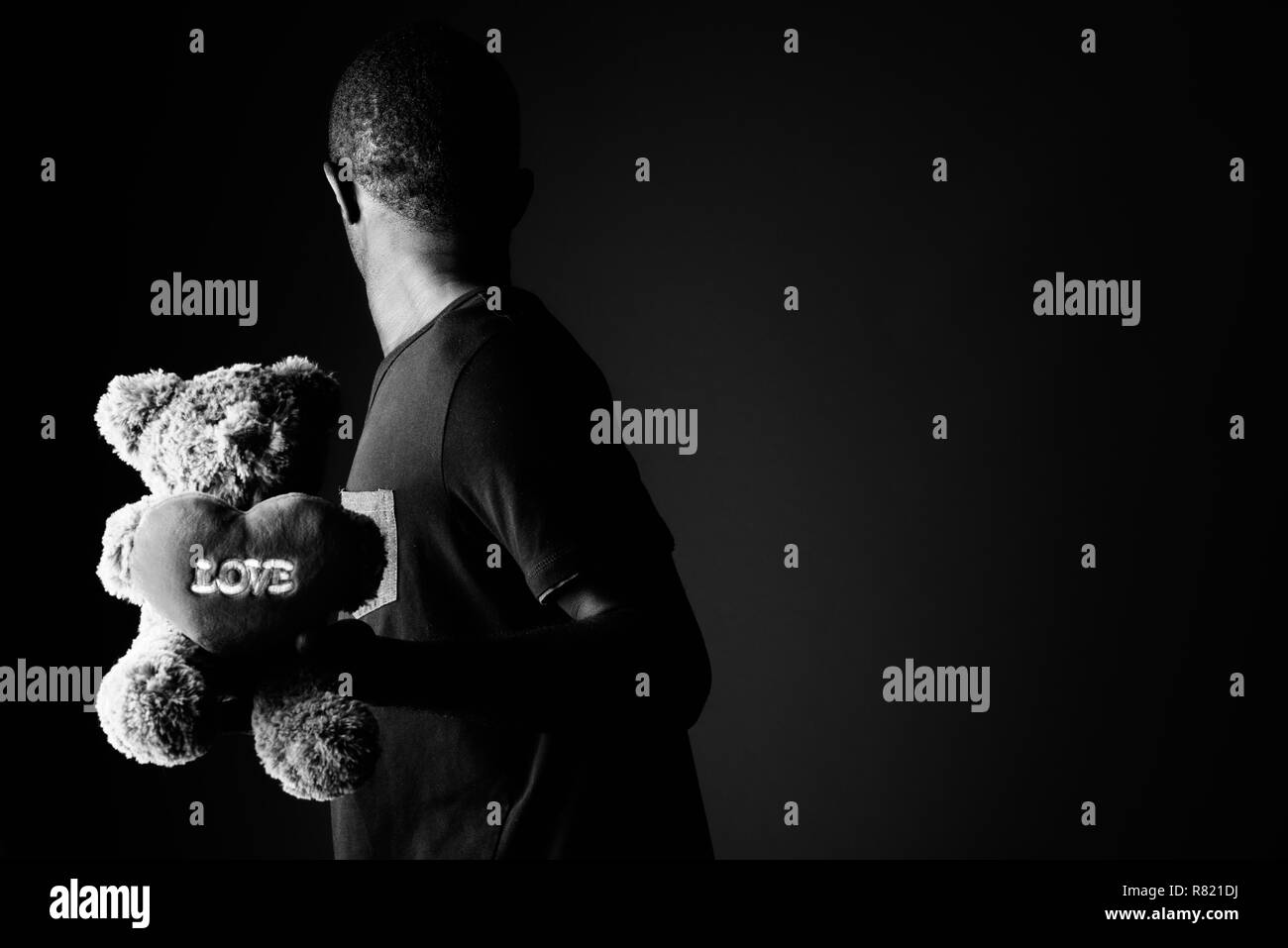 Sad young african man with teddy bear and love sign text in black and white