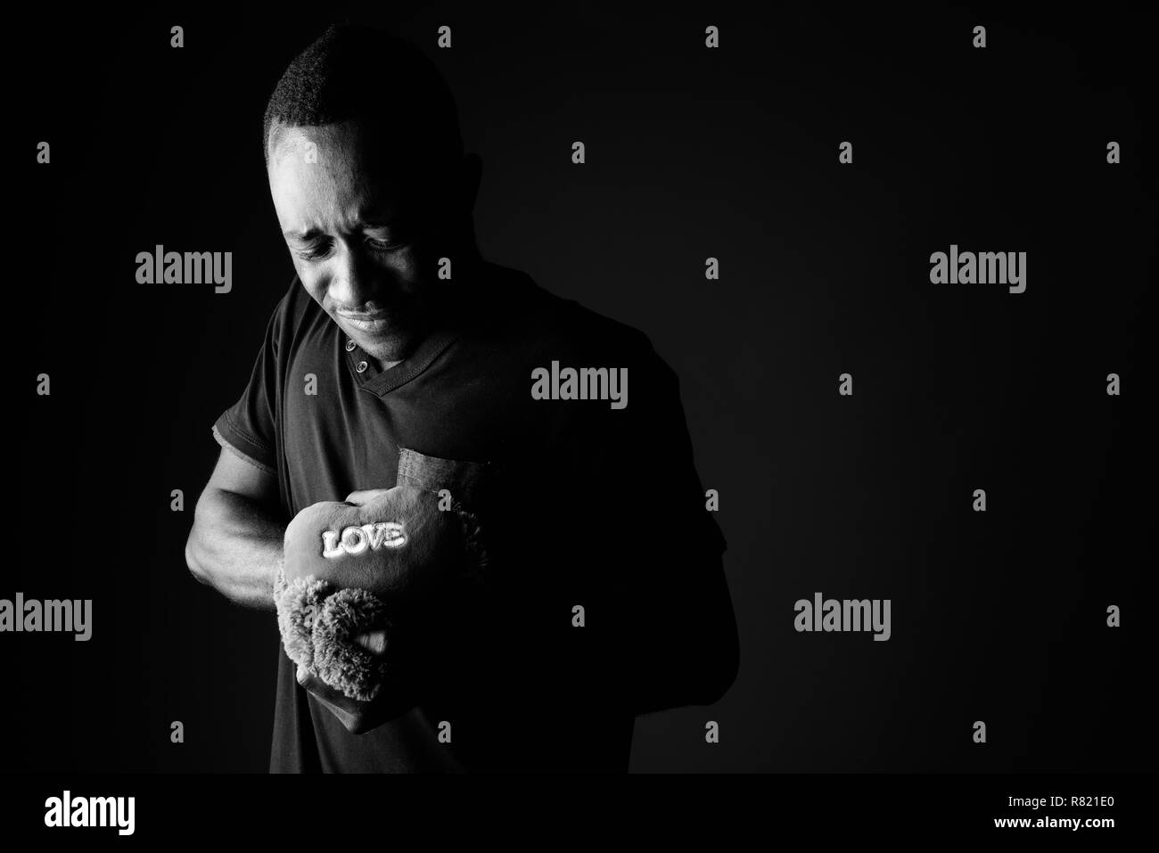 Sad young African man with teddy bear and love sign text in black and white Stock Photo