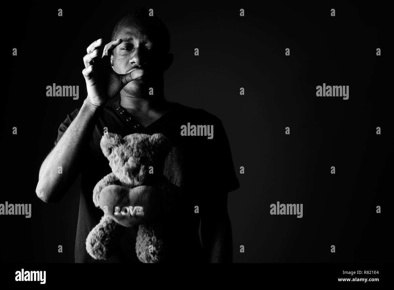 Sad depressed young African man with teddy bear and love sign text in black and white Stock Photo