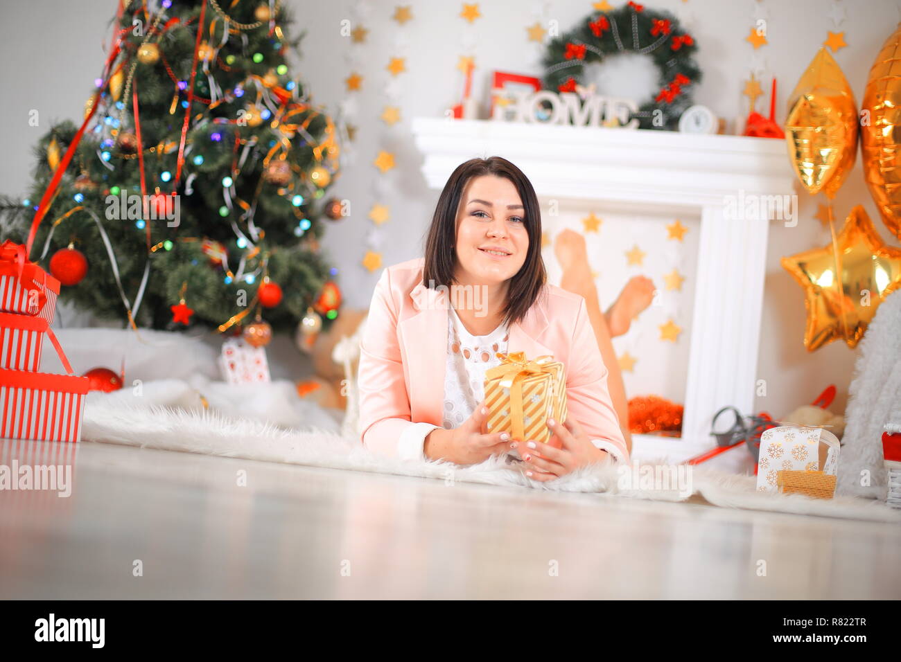 Happy young lady with curlu hair gifts by the fireplace near the Christmas tree. New year concept. Stock Photo