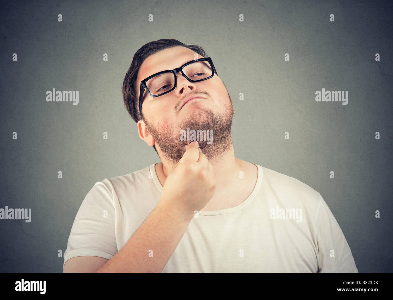 Adult chubby man in glasses rubbing double chin looking away and thinking on gray background Stock Photo