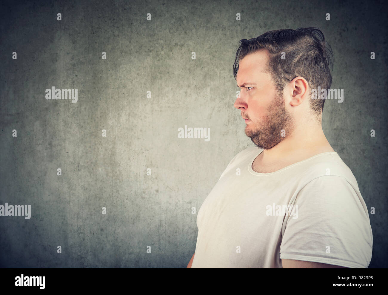 Side view of overweight casual man looking away in annoyance and disgust on gray background Stock Photo