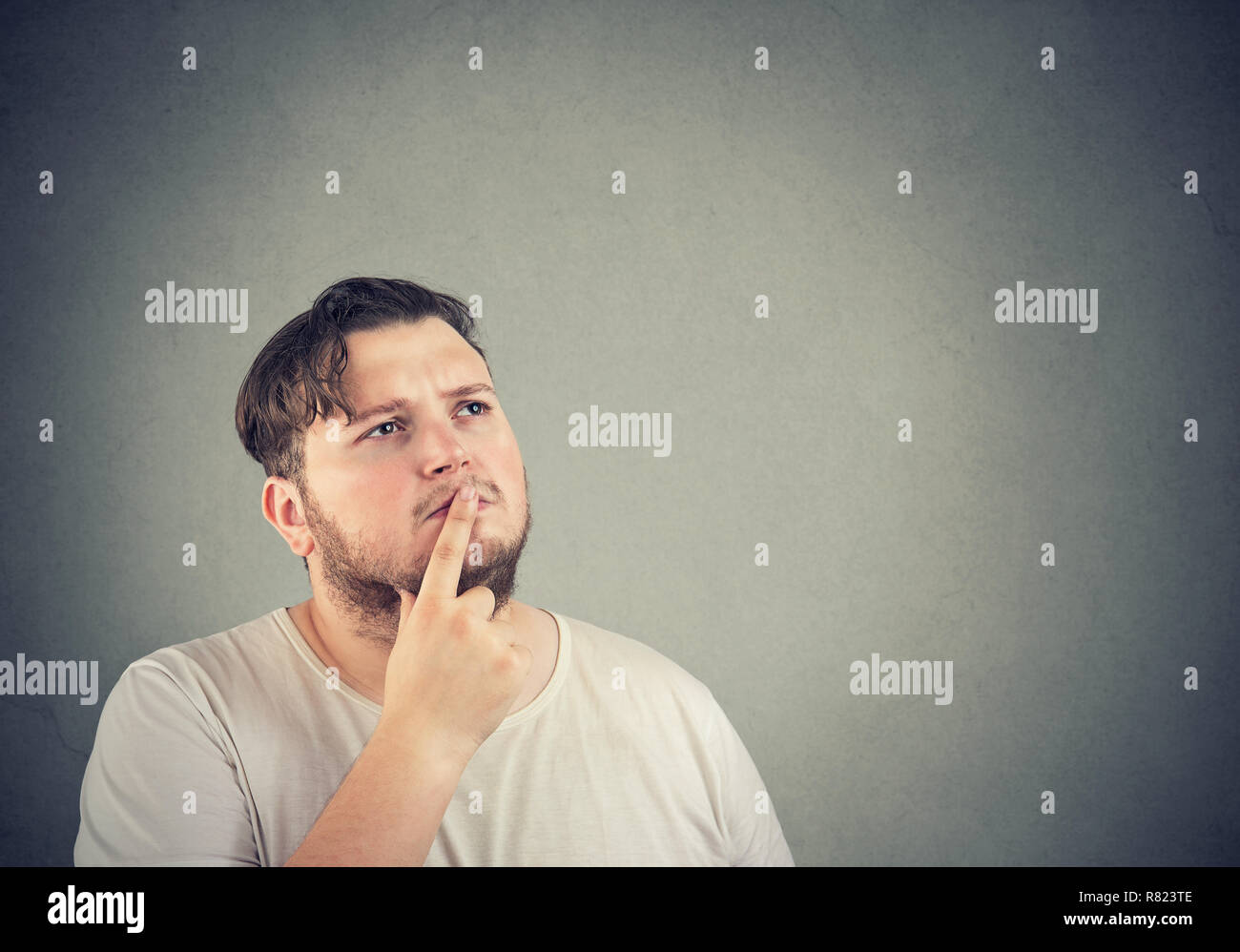 Adult chunky man touching lips with finger and looking away in deep thoughts making decision Stock Photo