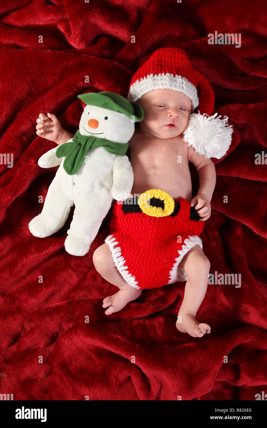 2 week old baby boy dressed as Santa with a snow man Stock Photo