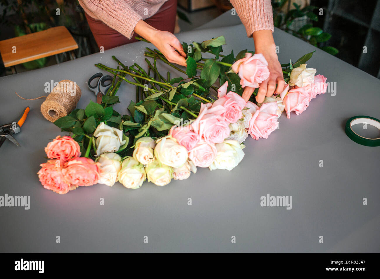 Picture of woman's hands putting roses together on grey table. Coil ...
