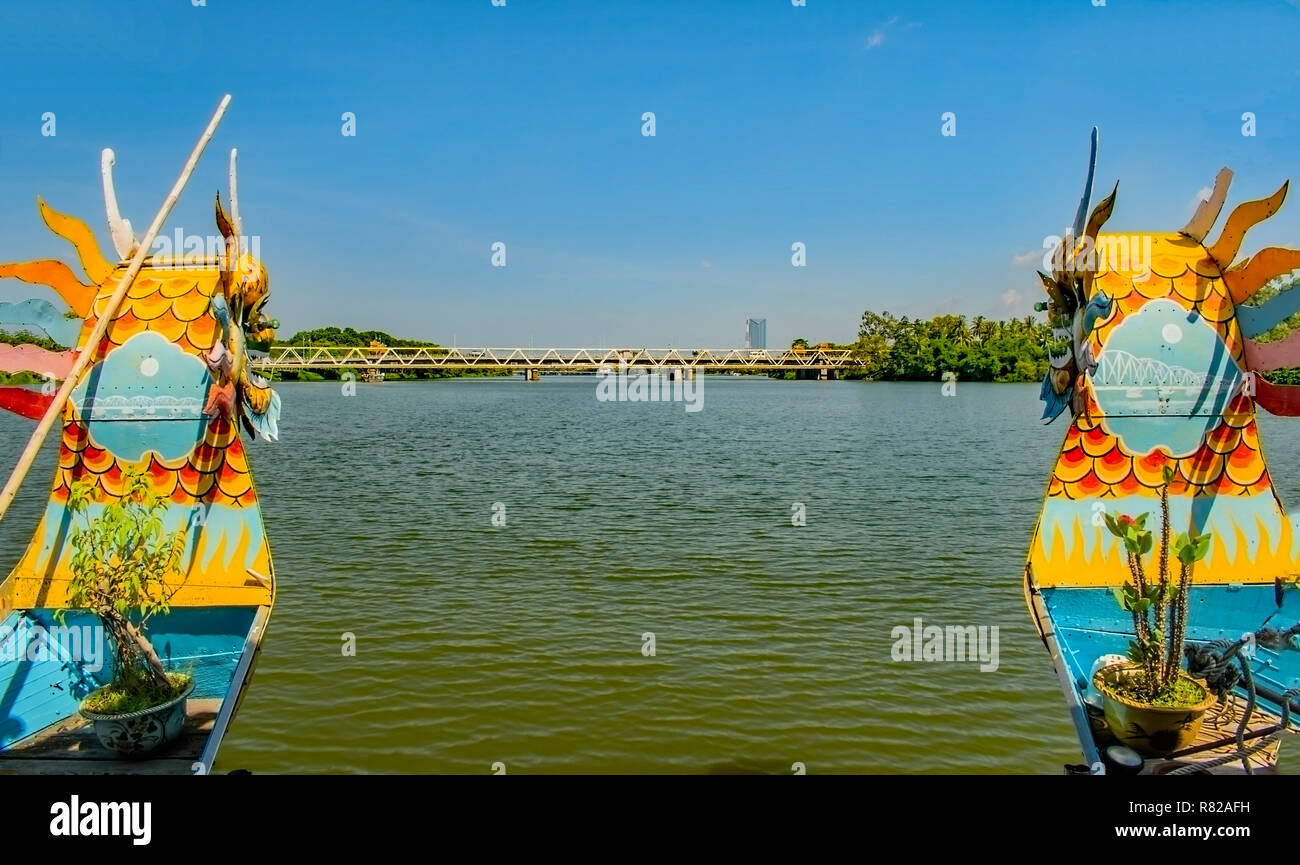 The two brightly painter prows of a dragonboat approaching a bridge on the Perfume River Hue,Vietnam. Stock Photo
