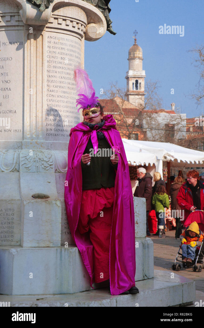 A young girl in carnevale fancy dress and mask poses by a statue in Campo Santa Margherita, Dorsoduro, Venice, Italy Stock Photo