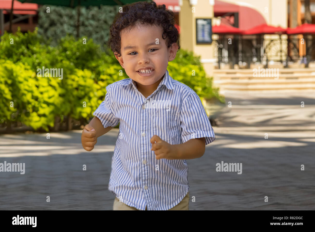 A little boy runs toward the camera with a smile.A  beautiful summer day at the town square a little boy has lots of room to run and burn off energy. Stock Photo