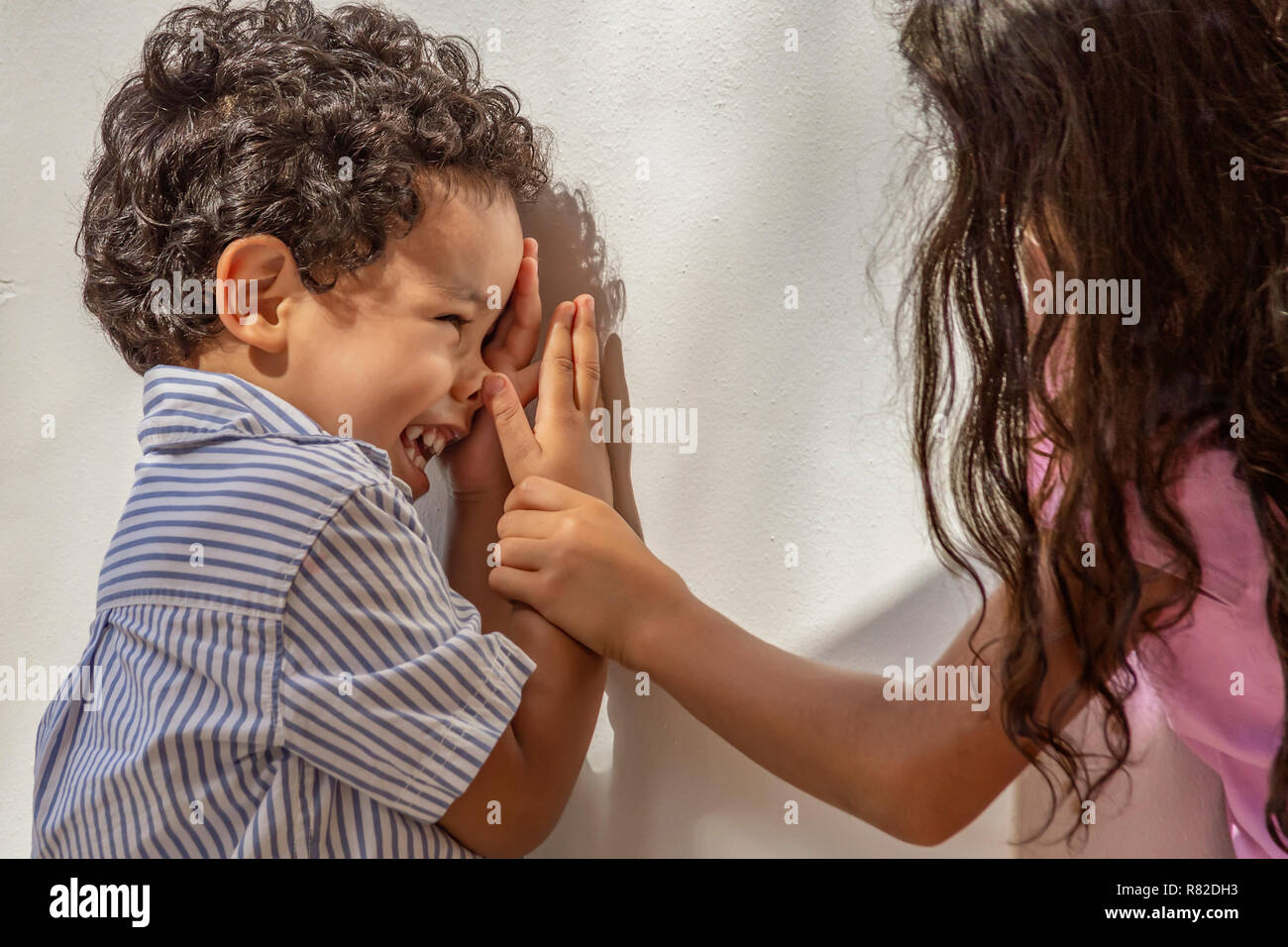 A little boy looks at his sister laughing as she grabs his arm. Playing with his older sister downtown outdoors at the community square. Stock Photo