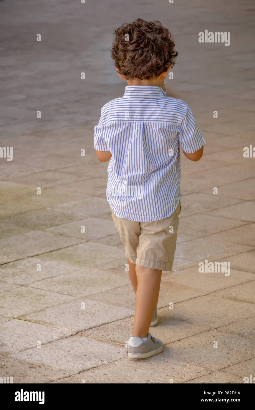 A Curly Hair Little Boy Confidently Leads The Way Up The Street A